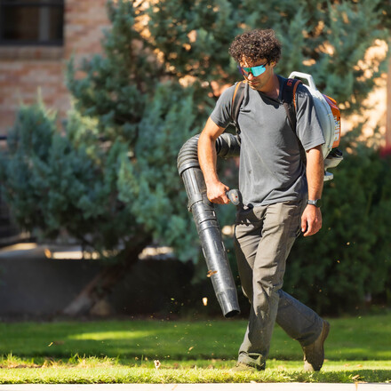 Grounds worker student using a leaf blower