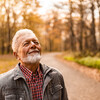 Tranquil senior man enjoying a walk on forest road on autumn day and breathing fresh air with eyes closed.