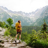 Happy woman with a yellow hiking backpack enjoying the mountain landscape. A young traveler travels along mountain paths. Adventure, travel concept.