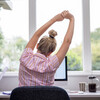 Rear View Of Woman Working From Home On Computer  In Home Office Stretching At Desk