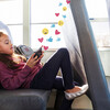 Young schoolgirl relaxes on the school bus. She is checking her social media account on her smartphone. Graphics of emojis, like buttons and heart symbols flow out from her smartphone.