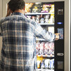 Hipster style man viewed from back buying snacks or drink from vending automatic machine typing product code. People and travel concept lifestyle