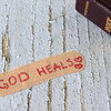 God heals, handwritten text on bandage with closed holy bible book on wooden background. Christian biblical concept of mercy, love, compassion and grace.