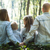 A family of four, husband, wife, son, and daughter, sitting in nature with their back to the camera.