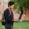 A college student walking outside using a laptop on the go.