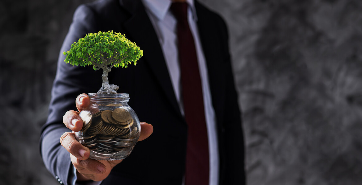 businessman holding jar of coin with small tree growing up