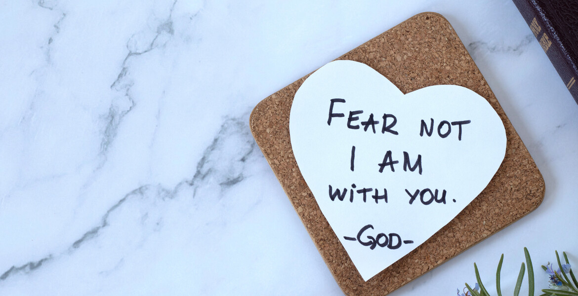 Fear not, I am with you, handwritten verse on heart-shaped note and closed holy bible book. Top table view. Copy space. Words of encouragement and hope from God Jesus Christ, Isaiah 41:10.