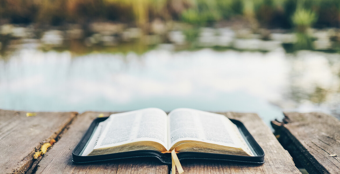 Open Bible on a wooden board near the river.