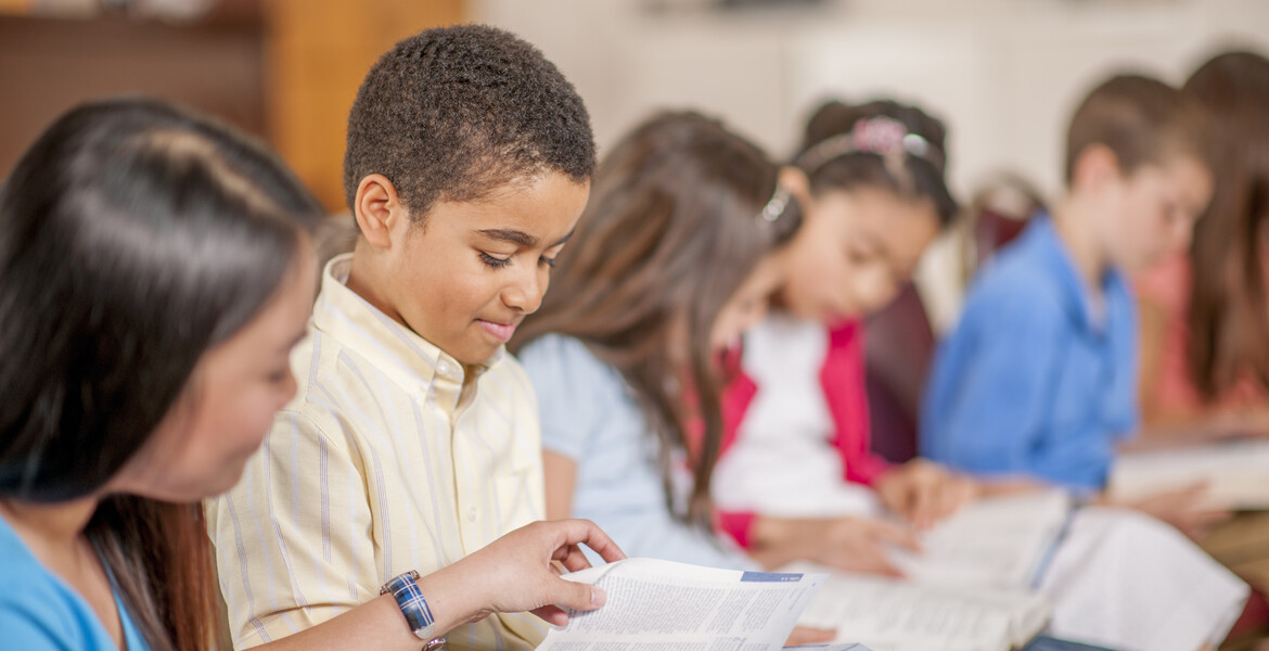 A multi-ethnic group of elementary age children are sitting together and are reading the Bible.