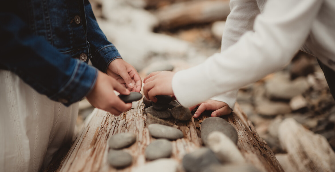Little girls stacking stones on a piece of driftwood at the beach