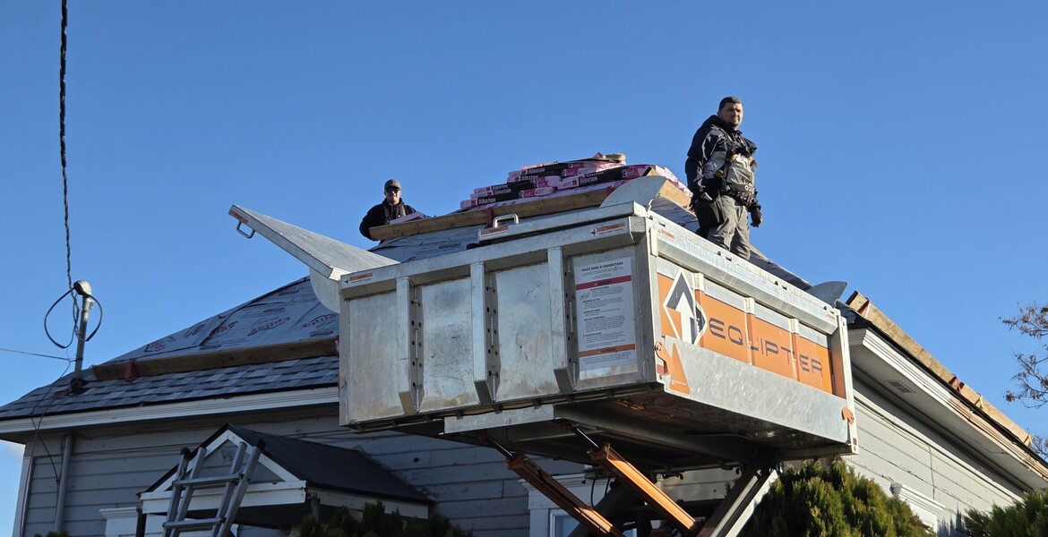 Two people stand on a scissor-lift and on the roof they are replacing with water-tight materials. 