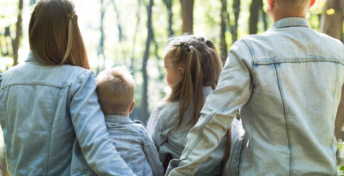 A family of four, husband, wife, son, and daughter, sitting in nature with their back to the camera.