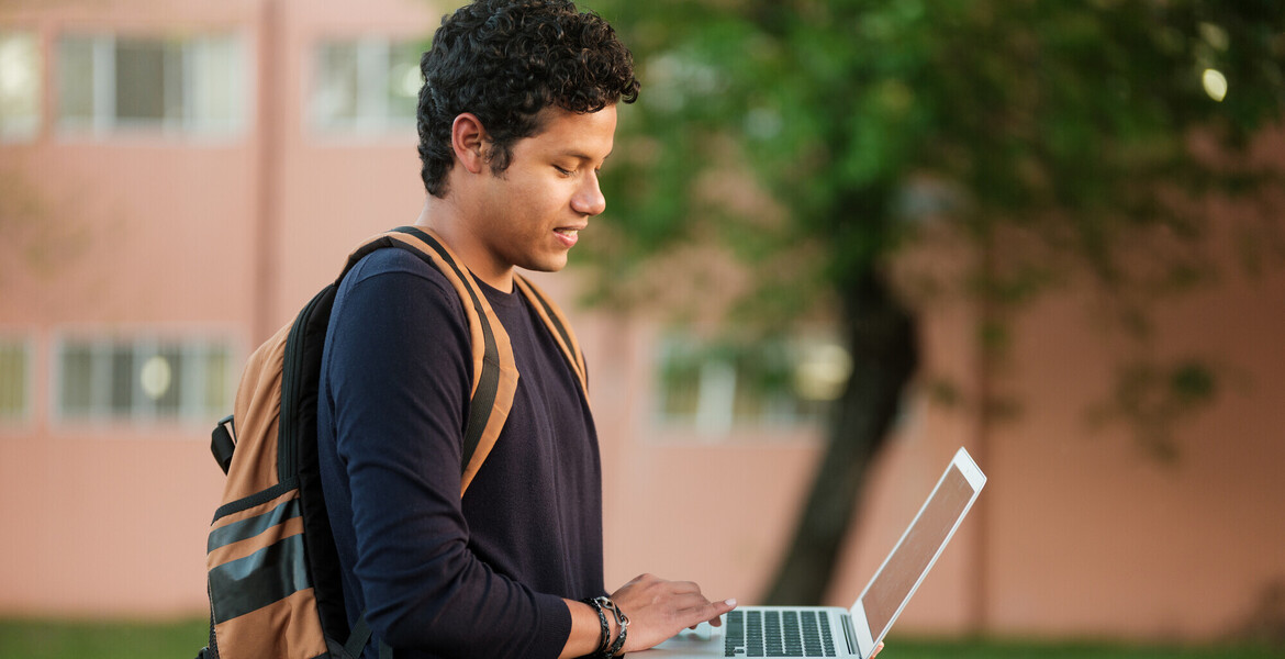 A college student walking outside using a laptop on the go.