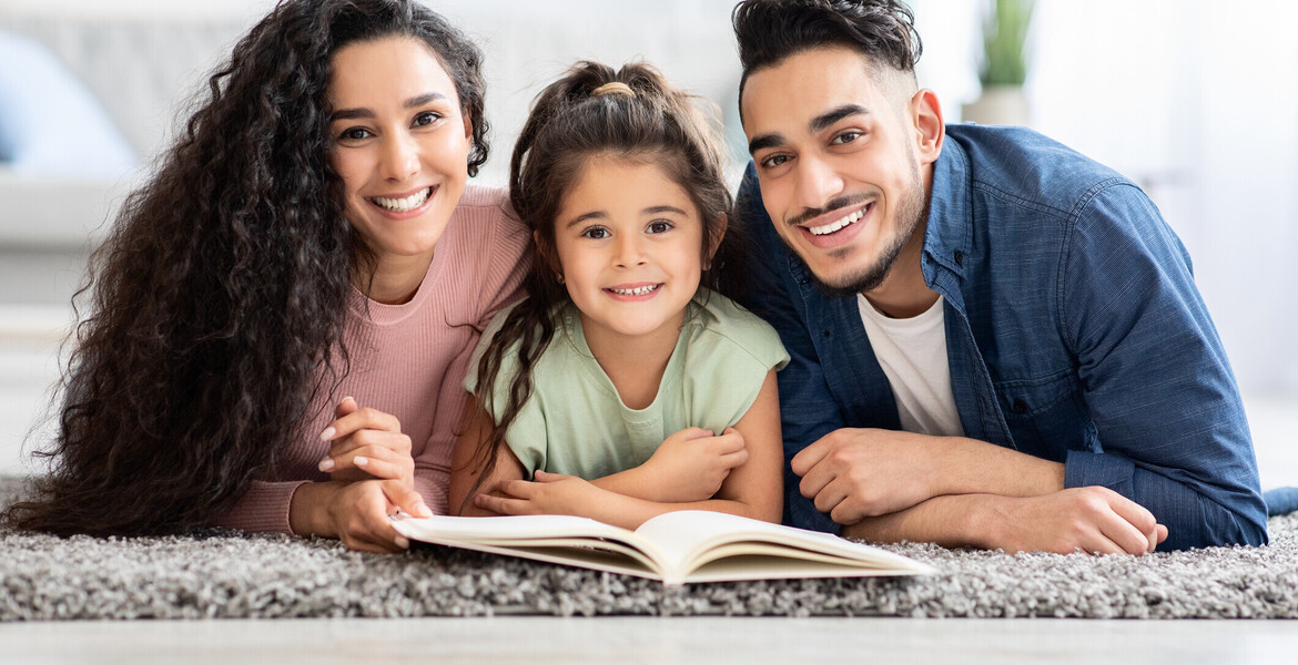Portrait Of Happy Parents Reading Book With Their Little Daughter