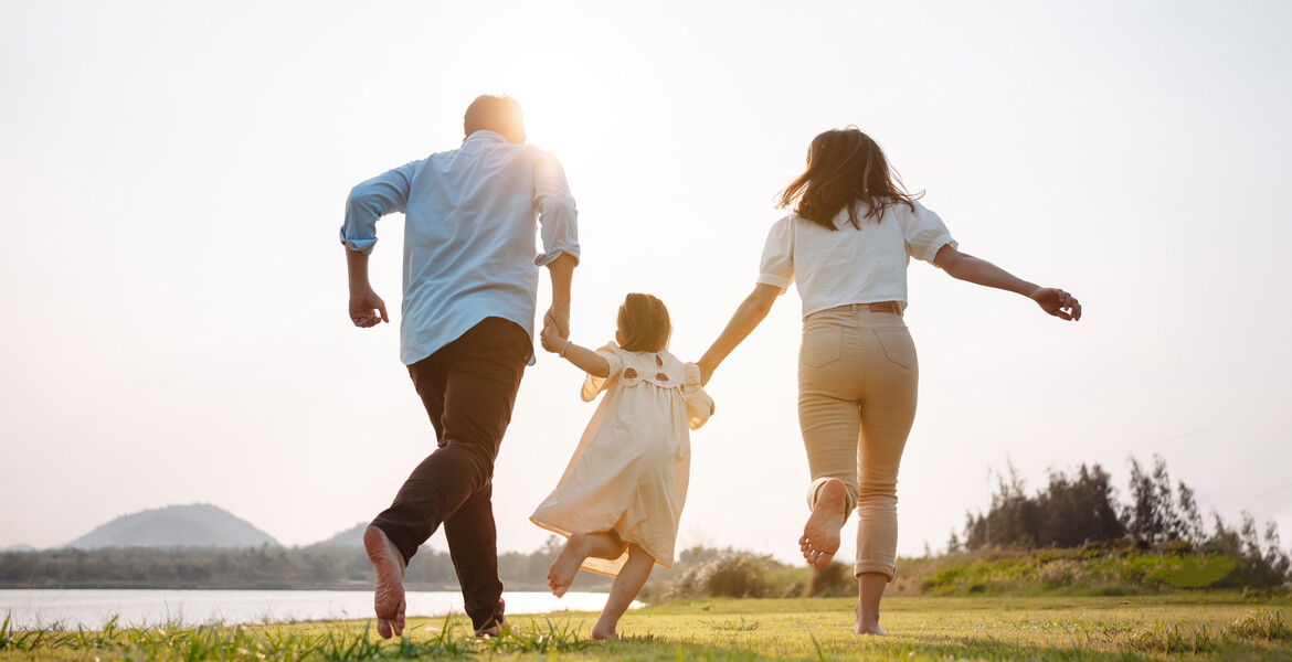 Happy family in the park sunset light. family on weekend running together in the meadow with river Parents hold the child hands.