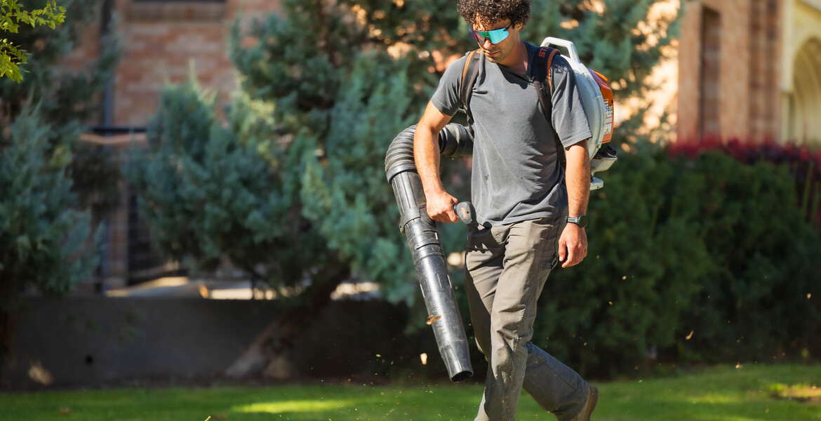 Grounds worker student using a leaf blower